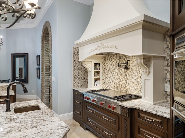 kitchen with stainless steel appliances, decorative backsplash, ornamental molding, a sink, and dark brown cabinets