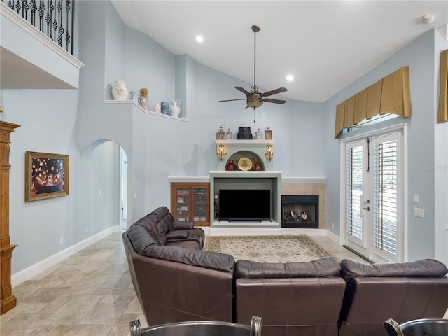 living area with arched walkways, ceiling fan, high vaulted ceiling, a tile fireplace, and baseboards