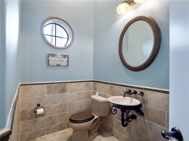 half bath featuring a wainscoted wall, a sink, toilet, and tile walls