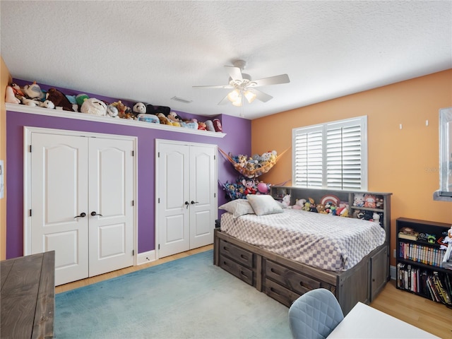 bedroom featuring a textured ceiling, a ceiling fan, visible vents, and multiple closets