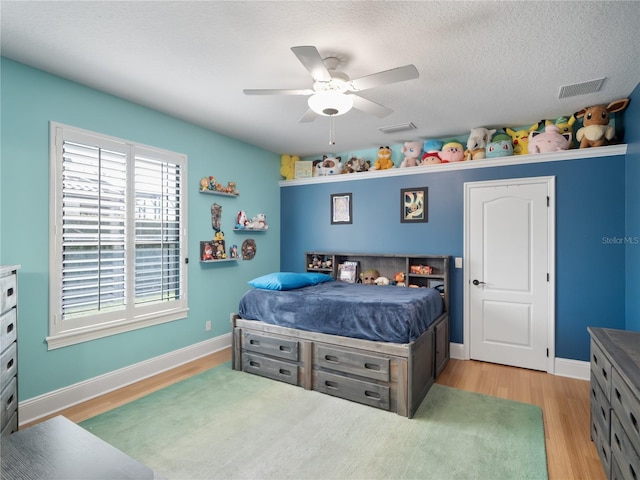 bedroom with a textured ceiling, light wood-type flooring, visible vents, and baseboards