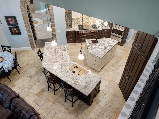 kitchen with a notable chandelier, stainless steel appliances, an island with sink, light stone countertops, and a kitchen breakfast bar