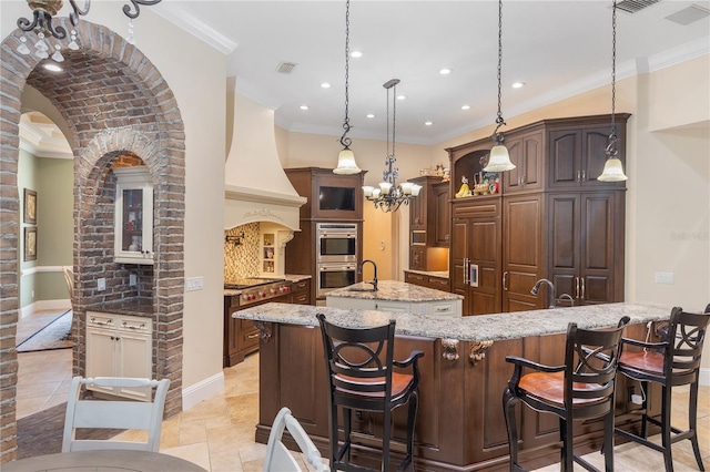 12860 Jacob Grace Ct, Windermere, FL 34786 - kitchen with a center island with sink, ornamental molding, appliances with stainless steel finishes, light stone counters, and a breakfast bar