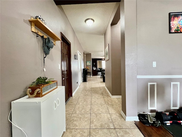 hall with a textured ceiling, baseboards, and light tile patterned floors