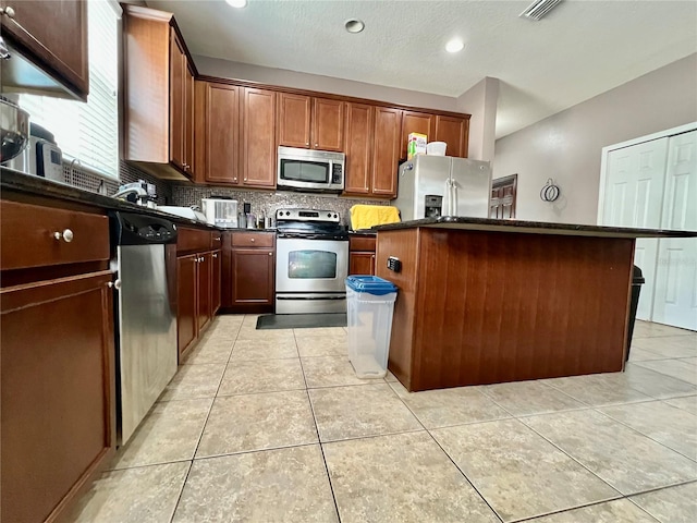 kitchen with light tile patterned floors, decorative backsplash, dark countertops, a kitchen island, and appliances with stainless steel finishes