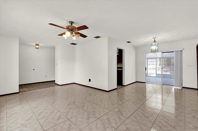 empty room featuring a textured ceiling, ceiling fan with notable chandelier, visible vents, and baseboards