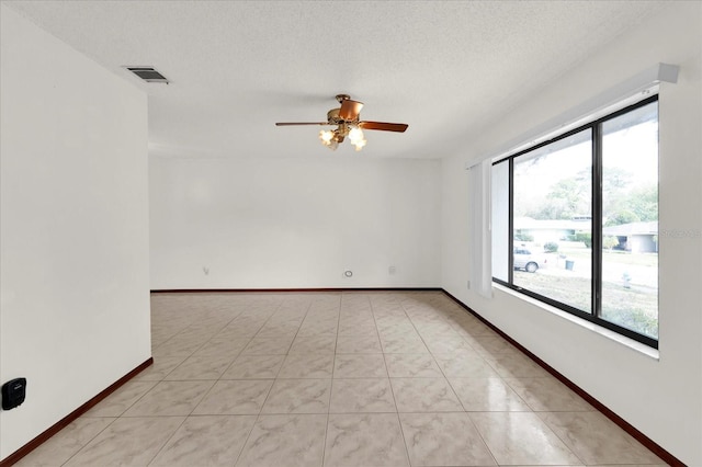 spare room with a textured ceiling, ceiling fan, a wealth of natural light, and baseboards