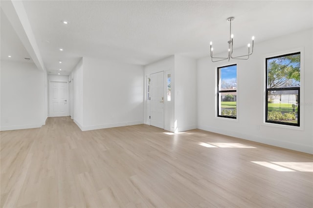 unfurnished living room with recessed lighting, light wood-style floors, a textured ceiling, a chandelier, and baseboards