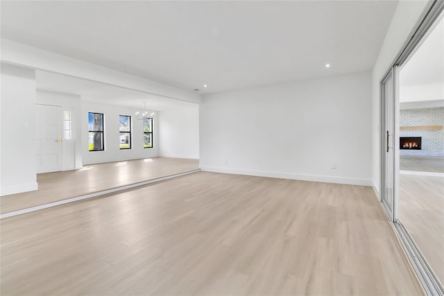 empty room with light wood-style floors, a large fireplace, and baseboards