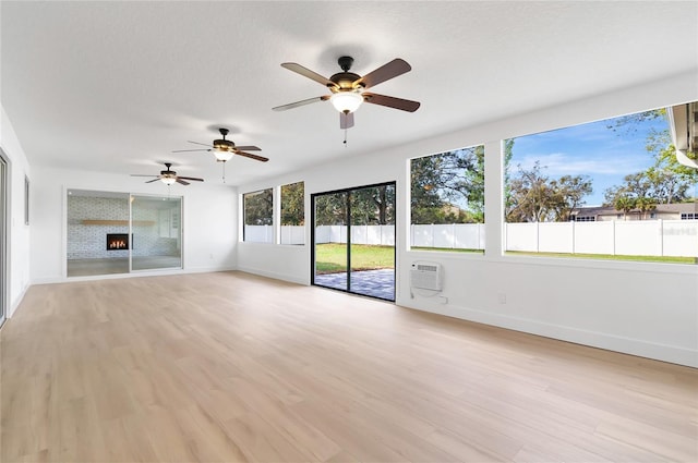 unfurnished living room with a warm lit fireplace, a textured ceiling, a wall unit AC, baseboards, and light wood-type flooring