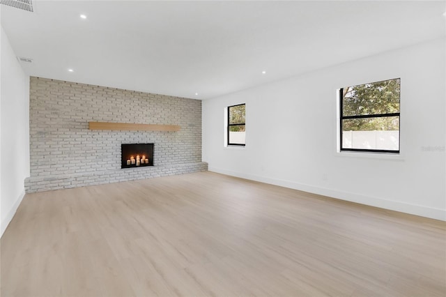 unfurnished living room with a brick fireplace, wood finished floors, visible vents, and baseboards