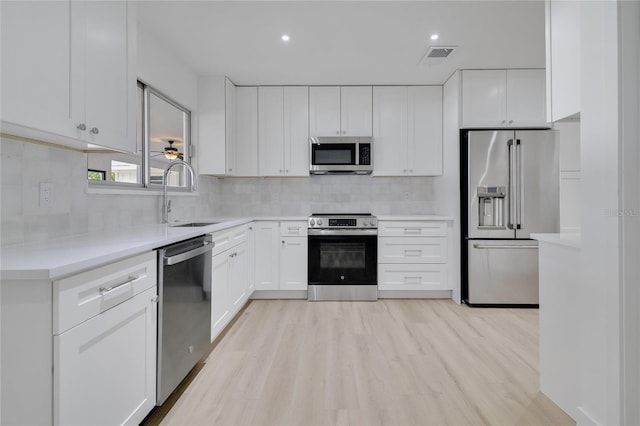 kitchen with appliances with stainless steel finishes, a sink, white cabinetry, and tasteful backsplash