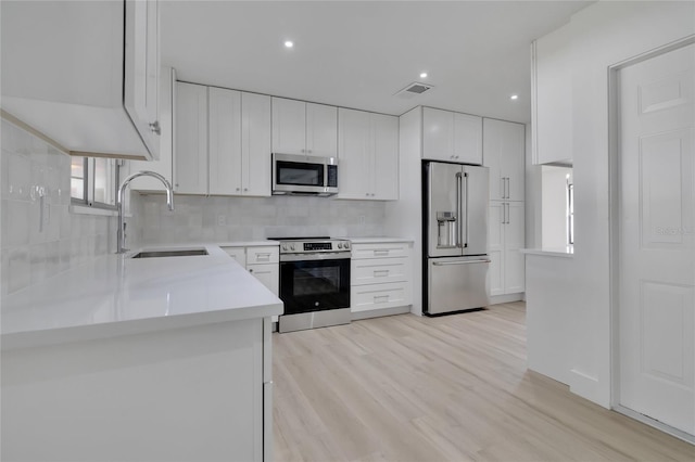 kitchen with a sink, visible vents, white cabinets, appliances with stainless steel finishes, and light wood finished floors