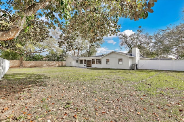 back of house featuring a fenced backyard, a chimney, and a lawn