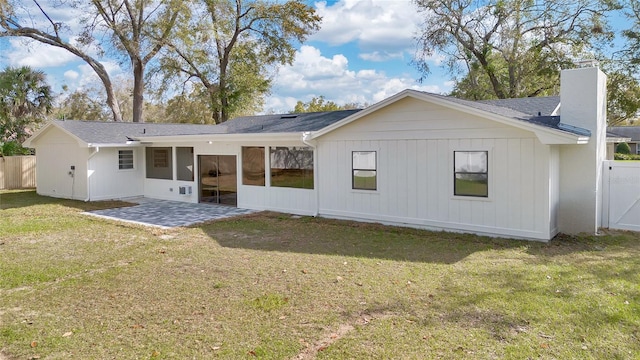 rear view of house featuring a patio, a chimney, a lawn, a sunroom, and fence