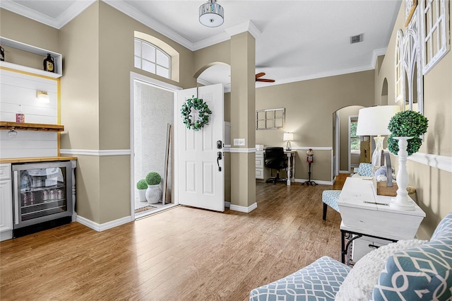 entrance foyer with ornamental molding, a ceiling fan, beverage cooler, and wood finished floors