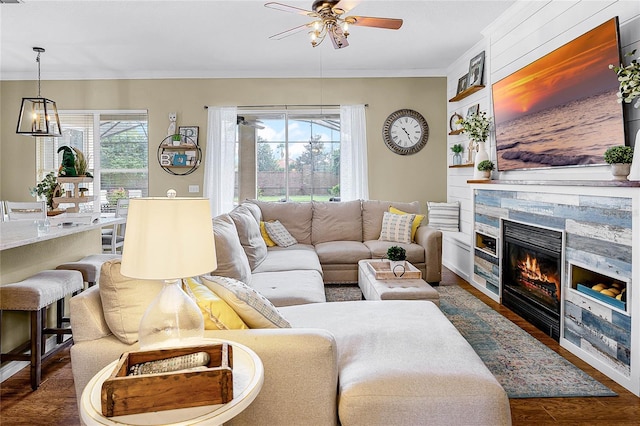 living area with a ceiling fan, dark wood-style flooring, a fireplace, and crown molding