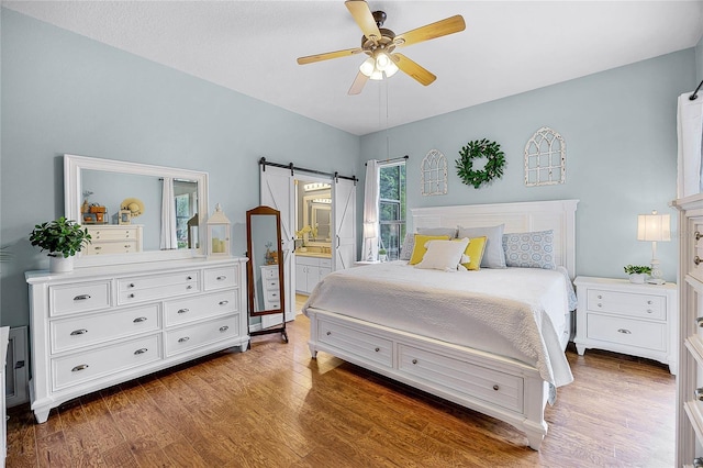 bedroom featuring a barn door, ceiling fan, wood finished floors, and ensuite bathroom