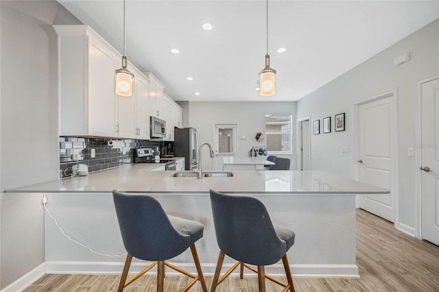 kitchen with appliances with stainless steel finishes, a peninsula, a sink, light wood-style floors, and backsplash