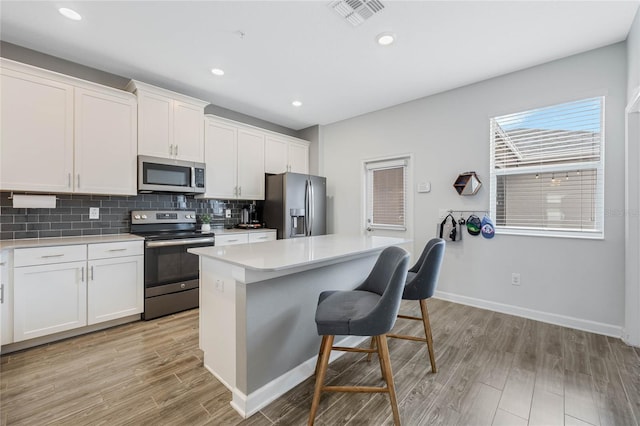 kitchen with visible vents, a kitchen island, stainless steel appliances, a kitchen bar, and backsplash