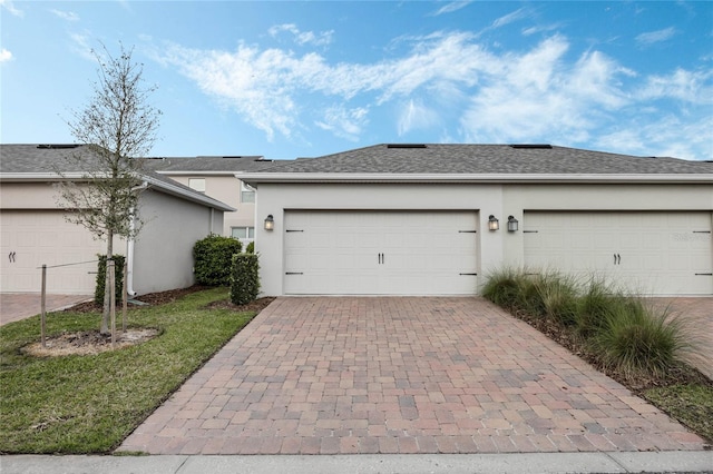 view of front of property with an attached garage, roof with shingles, decorative driveway, and stucco siding