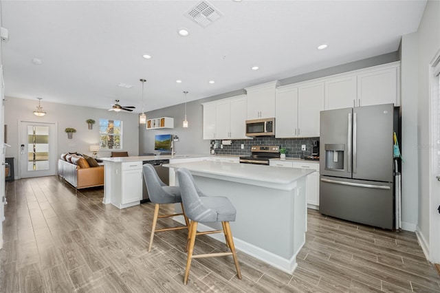 kitchen featuring stainless steel appliances, tasteful backsplash, light countertops, visible vents, and a peninsula