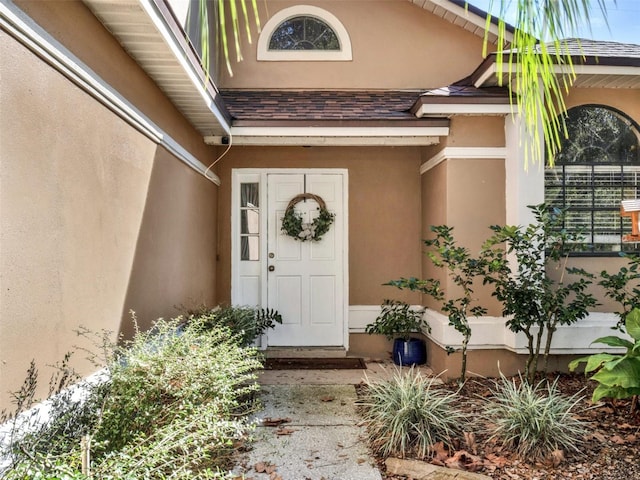 doorway to property with a shingled roof and stucco siding