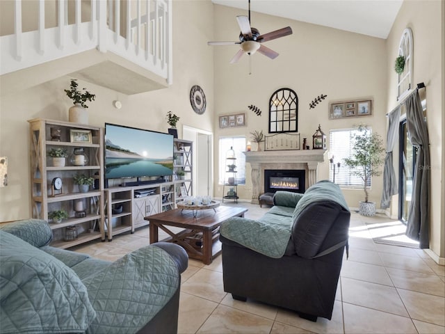 living room with ceiling fan, a high ceiling, light tile patterned flooring, and a glass covered fireplace