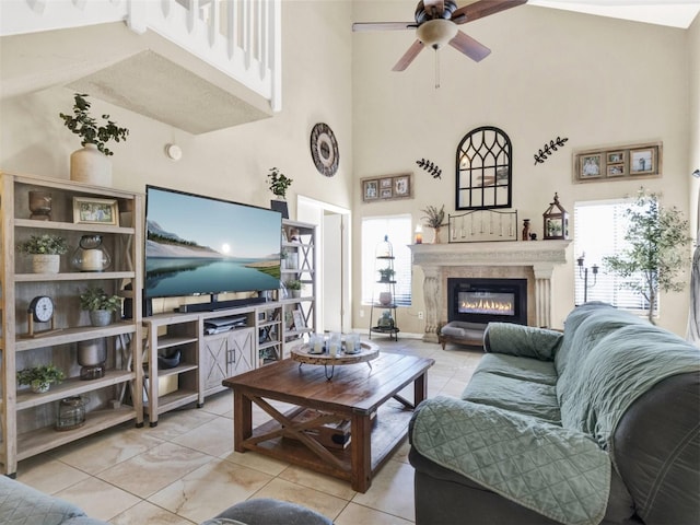 living area with a glass covered fireplace, ceiling fan, and a high ceiling