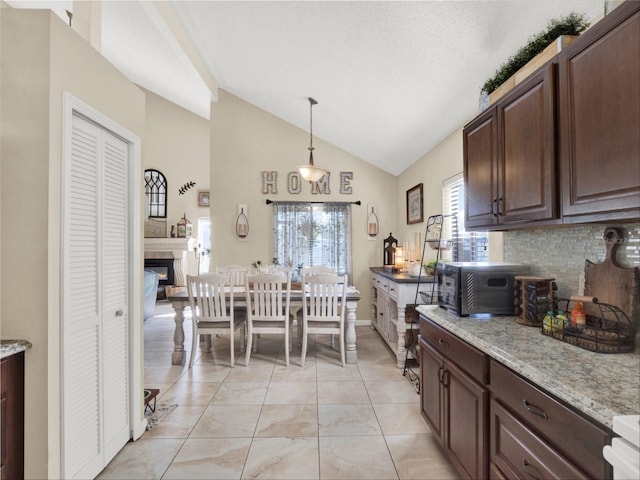 kitchen with vaulted ceiling, tasteful backsplash, a glass covered fireplace, and dark brown cabinetry