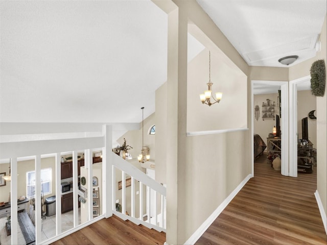 corridor with baseboards, wood finished floors, stairs, and a notable chandelier