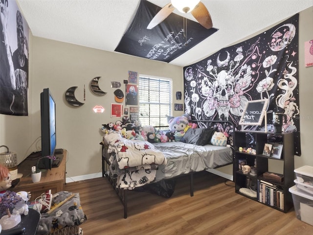 bedroom featuring ceiling fan, a textured ceiling, baseboards, and wood finished floors