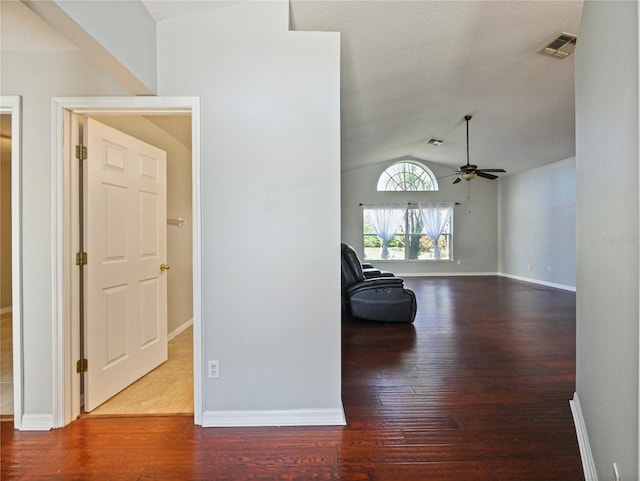 hallway featuring lofted ceiling, visible vents, baseboards, and wood finished floors