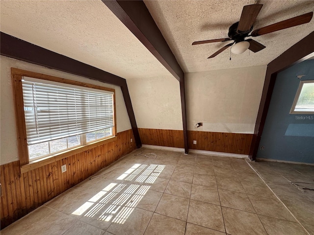 empty room with ceiling fan, a textured ceiling, wooden walls, a wainscoted wall, and tile patterned floors