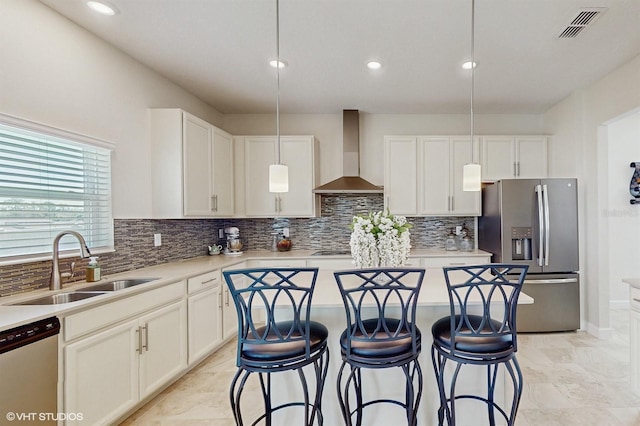 kitchen with visible vents, a breakfast bar area, appliances with stainless steel finishes, wall chimney range hood, and a sink