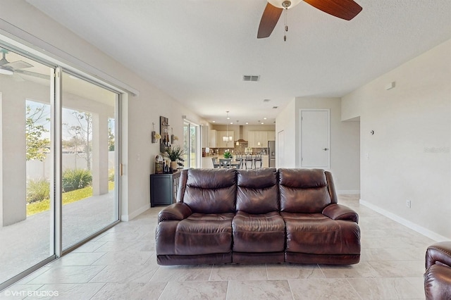 living room with baseboards, visible vents, and ceiling fan