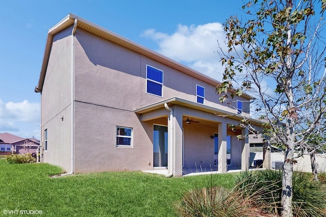 rear view of house featuring a ceiling fan, a lawn, and stucco siding