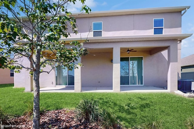 rear view of house with ceiling fan, a lawn, and stucco siding