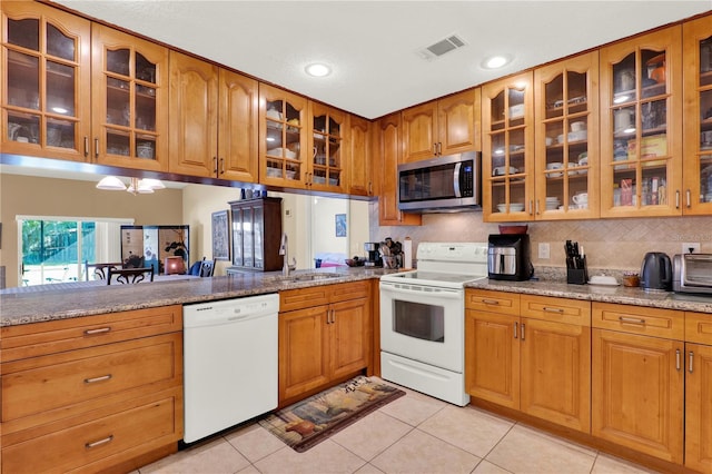 kitchen featuring white appliances, brown cabinetry, visible vents, a sink, and glass insert cabinets