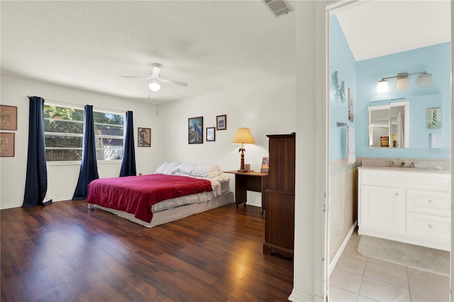 bedroom with a ceiling fan, wood finished floors, visible vents, a sink, and a textured ceiling