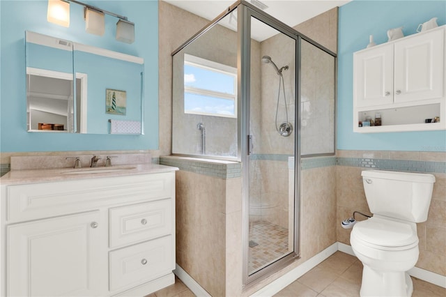 bathroom with vanity, a shower stall, tile walls, toilet, and tile patterned floors