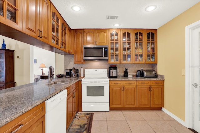 kitchen with brown cabinetry, white appliances, glass insert cabinets, and a sink