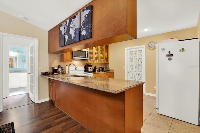 kitchen with brown cabinetry, a peninsula, freestanding refrigerator, stainless steel microwave, and range