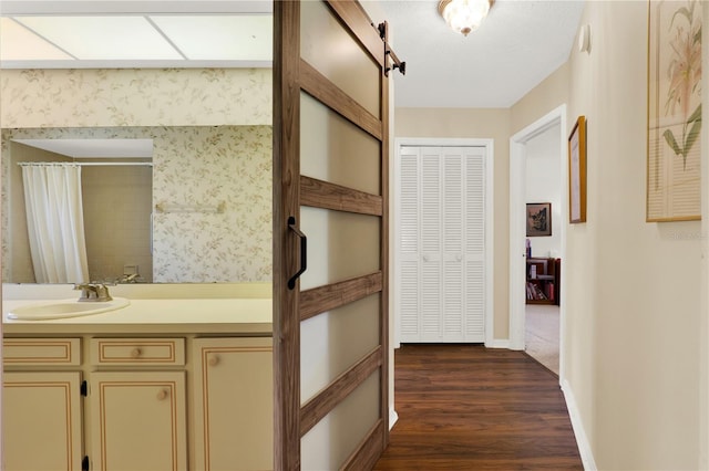 corridor with a sink, a barn door, baseboards, and dark wood-style floors