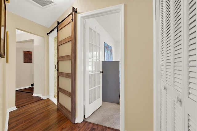 hallway featuring visible vents, baseboards, dark wood-type flooring, and a barn door