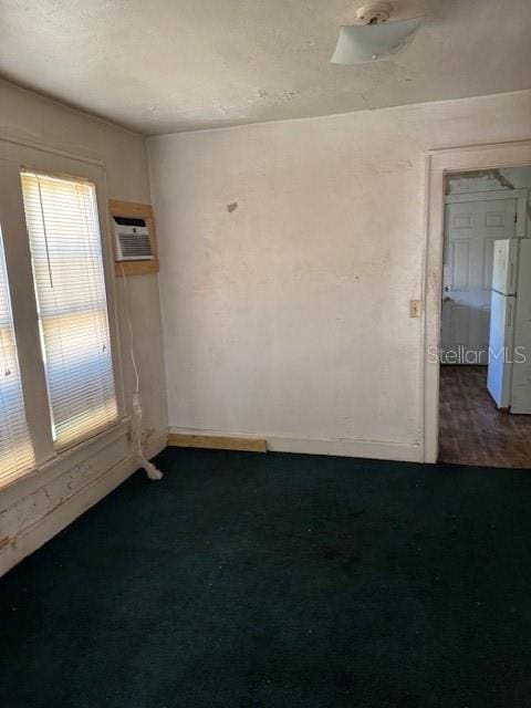 unfurnished room featuring dark colored carpet and a wall mounted air conditioner