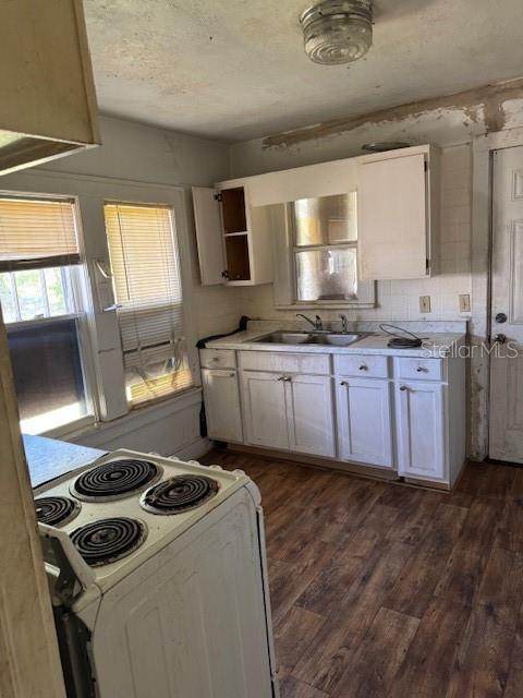 kitchen with white electric stove, white cabinets, dark wood-style floors, light countertops, and a sink