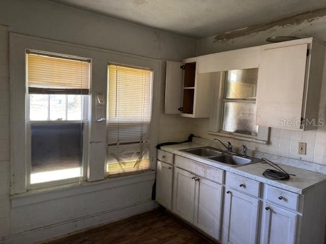 kitchen featuring white cabinets, decorative backsplash, dark wood-type flooring, light countertops, and a sink