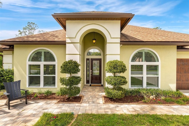 doorway to property with a patio area, roof with shingles, and stucco siding