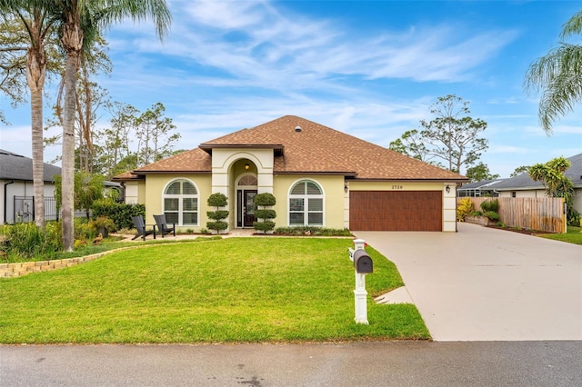 mediterranean / spanish home featuring a garage, fence, concrete driveway, stucco siding, and a front lawn